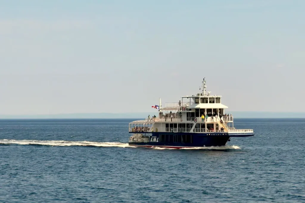 A white and blue AML cruise ship sails across calm waters, carrying passengers on a whale watching excursion for a pre-bex tour under a clear sky.