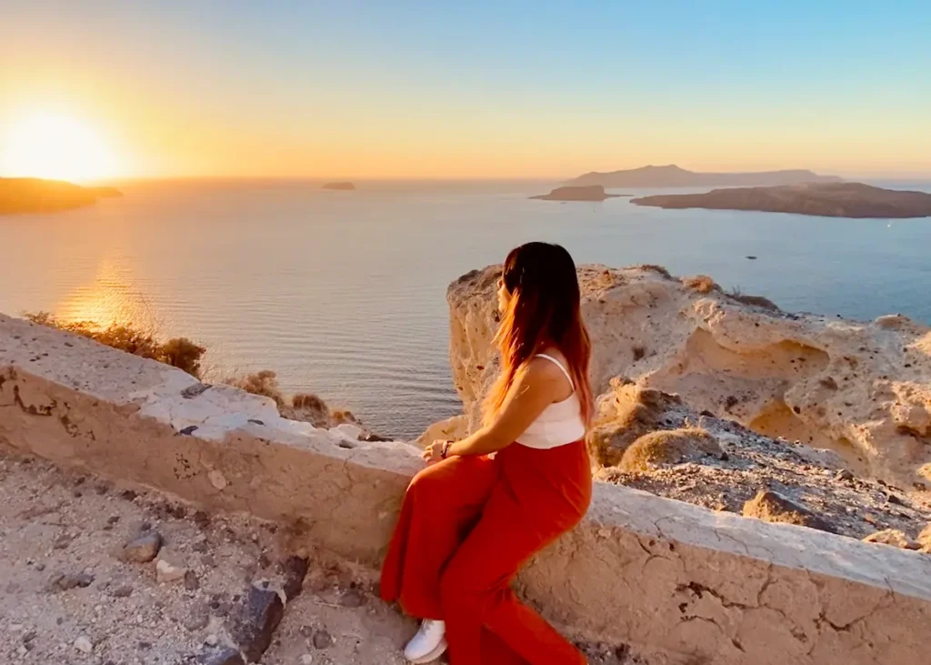 Solo traveler watching a colorful sunset over the sea cliffs in Santorini, a peaceful and memorable solo travel activity.