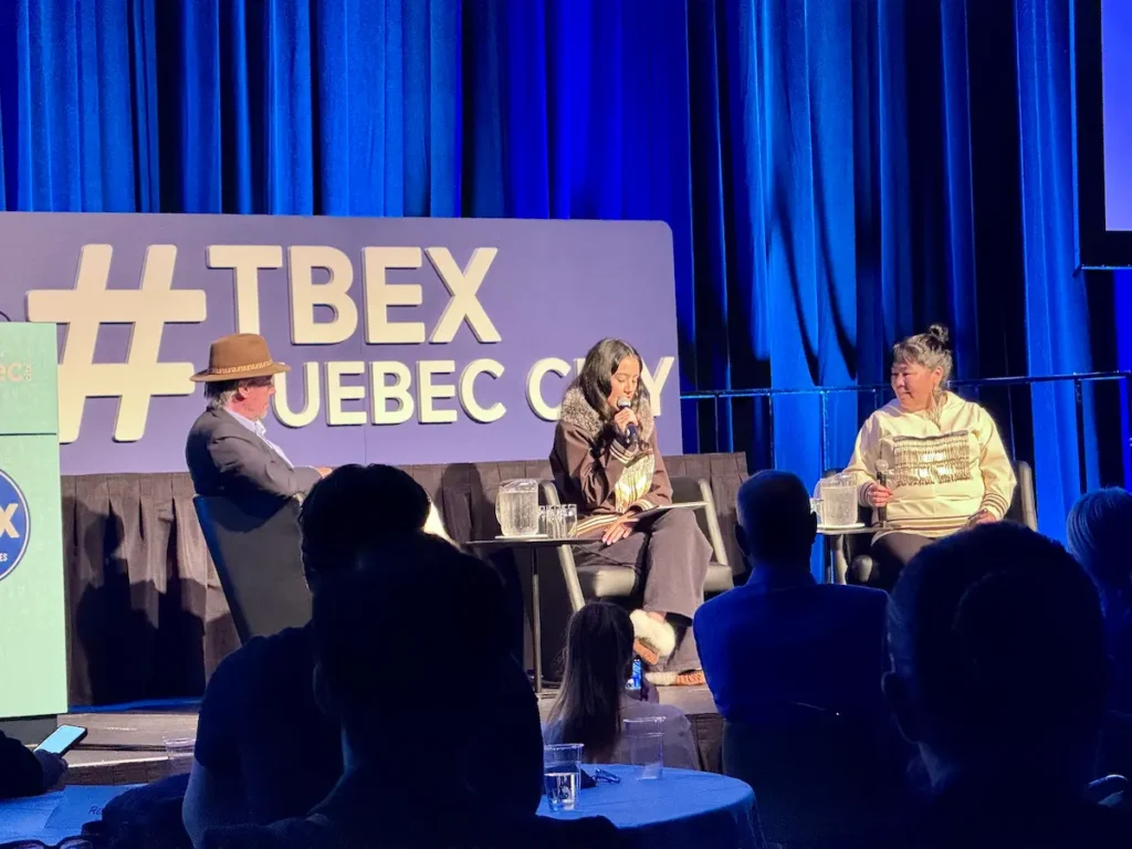 Three TBEX keynote speakers sit on stage at TBEX Quebec City, engaging in a discussion before an audience.